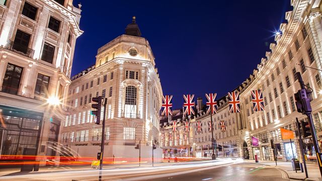 Regent Street is one of the most famous and popular places to shop in London. Image courtesy of Shutterstock. View of Regents Street at night with row of Union Jack flags.