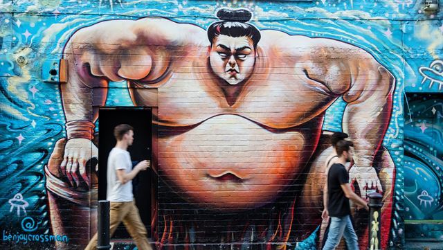 Graffiti mural of a sumo wrestler on Brick Lane. Image courtesy of visitlondon.com/Jon Reid. Graffiti mural of a sumo wrestler against a blue background on a brick wall in Spitalfields.