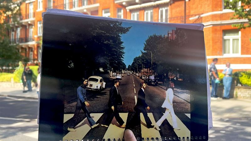 A photograph of the Abbey Road album cover is held up in front of the famous crossing.