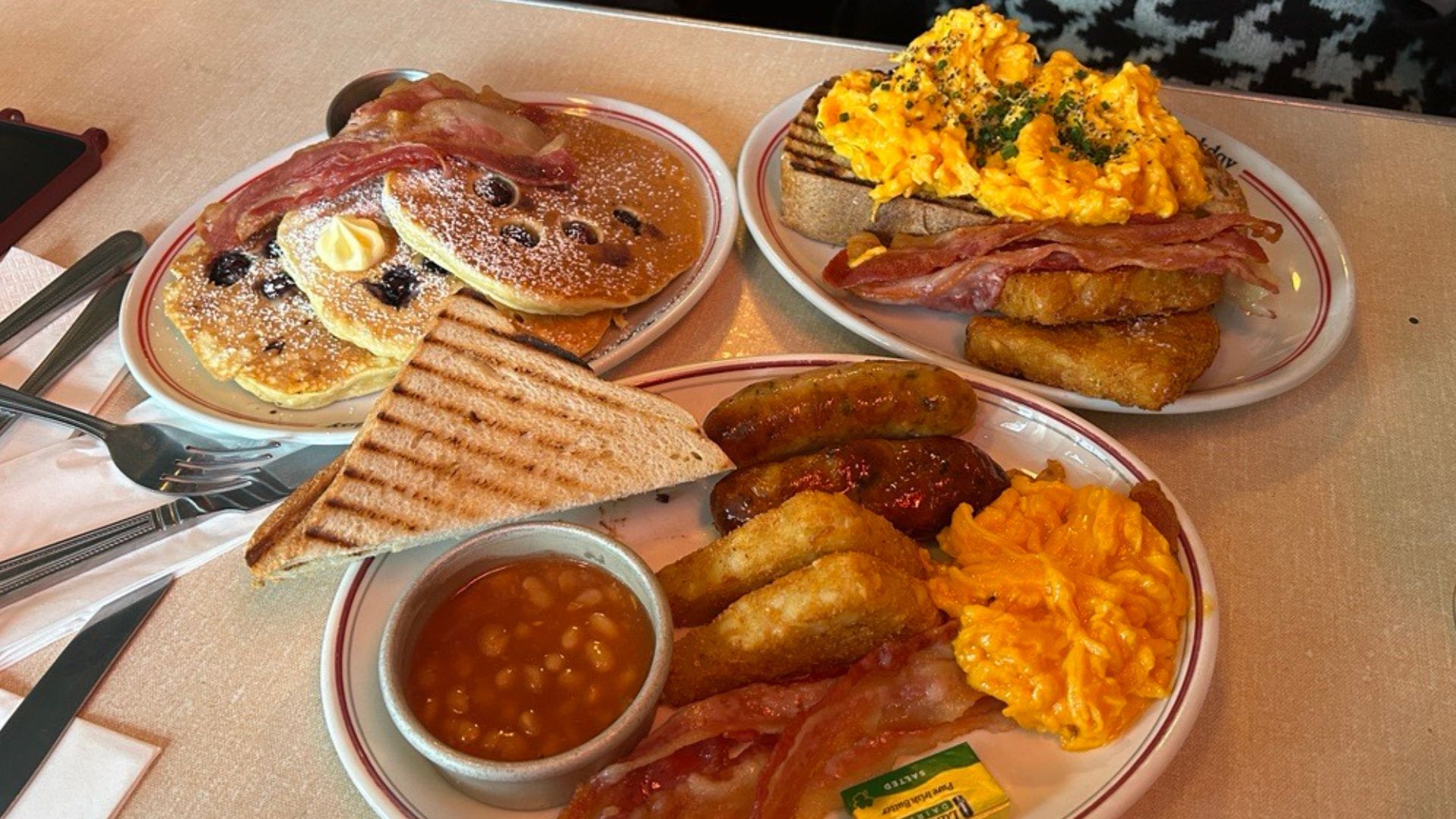 Tuck into a tasty English breakfast spread at The Breakfast Club. © Visit London/Hannah Cornish three plates of breakfast food including full english breakfast, scrambled egg on toast and pancakes with berries