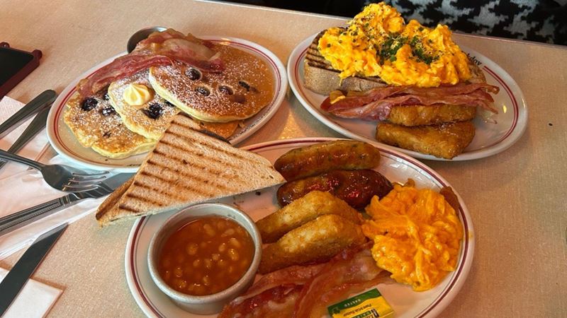 Tuck into a tasty English breakfast spread at The Breakfast Club. Credit: Hannah Cornish. Image courtesy of Visit London. three plates of breakfast food including full english breakfast, scrambled egg on toast and pancakes with berries