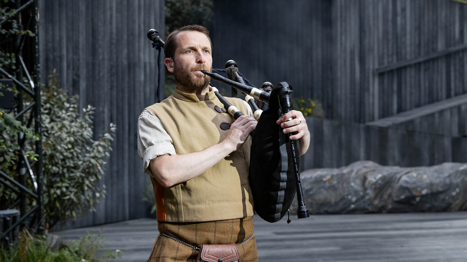 David Colvin as Angus & Piper in Brigadoon at Regent's Park Open Air Theatre. Image courtesy of London Theatre Direct/Mark Senior. A man plays the bagpipes in the opening of Brigadoon
