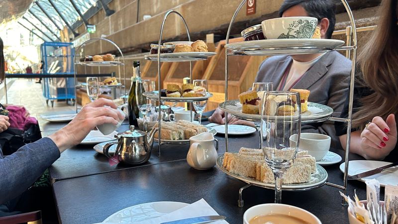 people sat a dark long table with tiered afternoon stands with sweet and savoury treats, and cups of tea and glasses of prosecco on the table