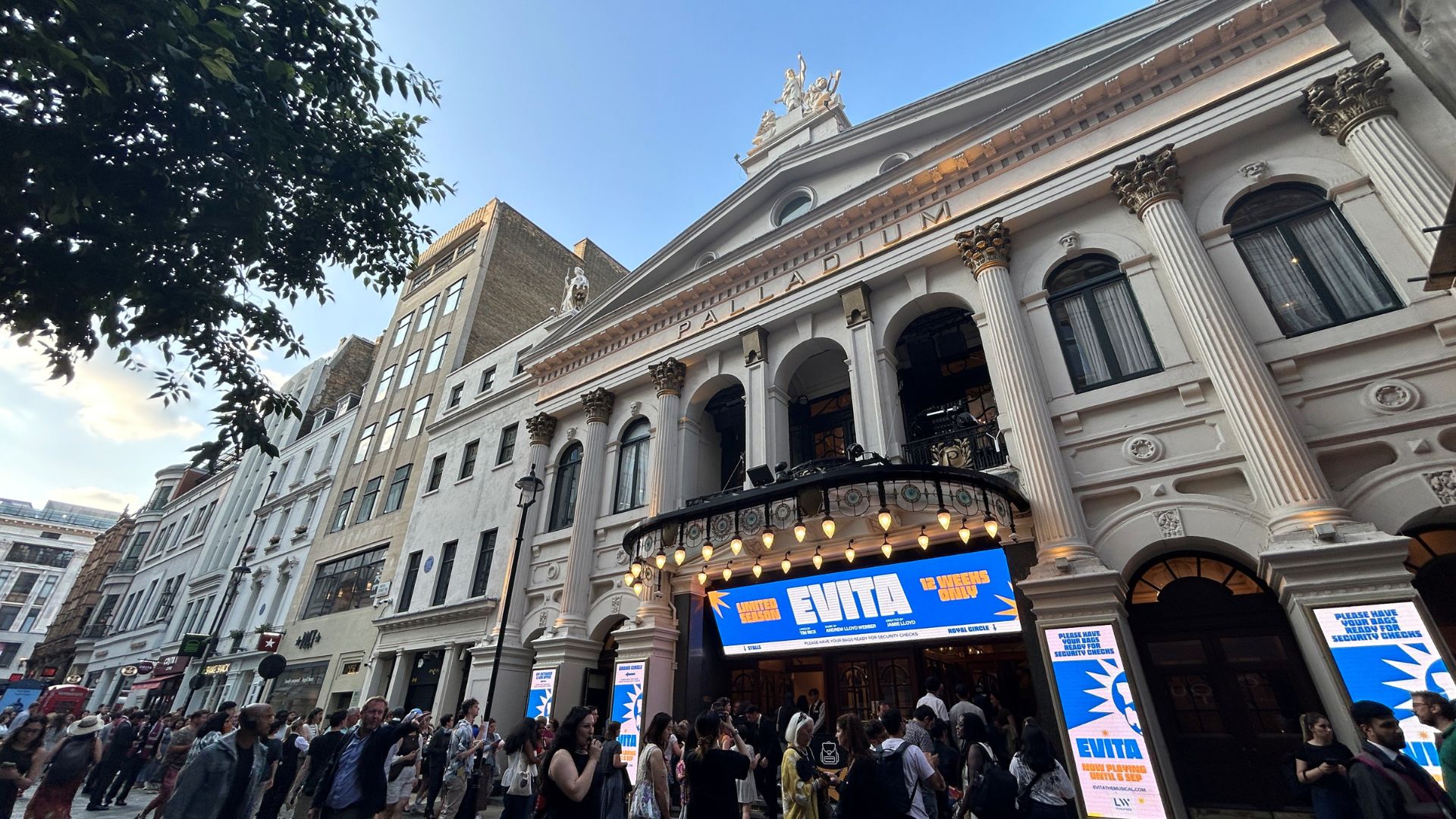 Experience a reimagined classic and bold new adaptation of Evita at The London Palladium. Photo credit: Hannah Cornish wide angle photo of the exterior of The London Palladium theatre, with Evita signage at the front and crowds queuing to enter the theatre