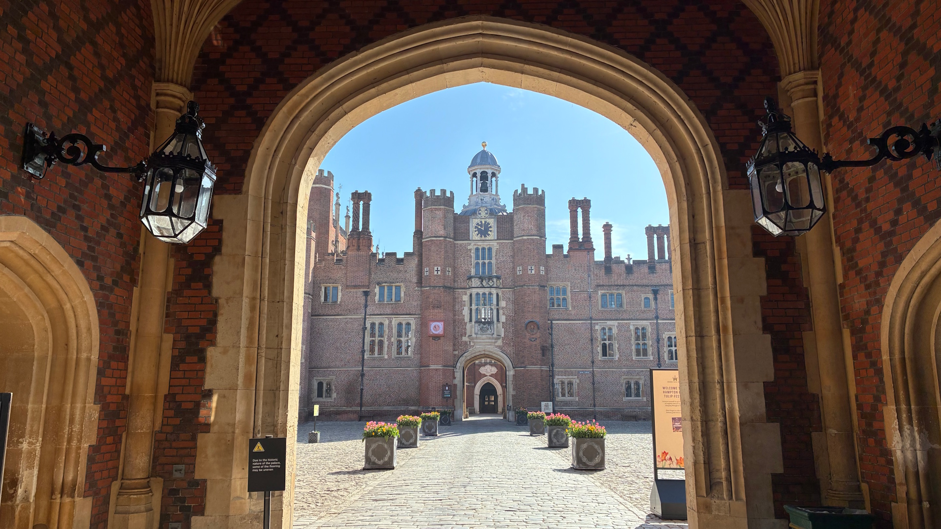 See displays of tulips in Hampton Court Palace's courtyards, including the Base Court © visitlondon.com. Image courtesy of Jonny Payne. A view through an arched doorway into the Base Court at Hampton Court Palace, which boasts planters full of tulips.