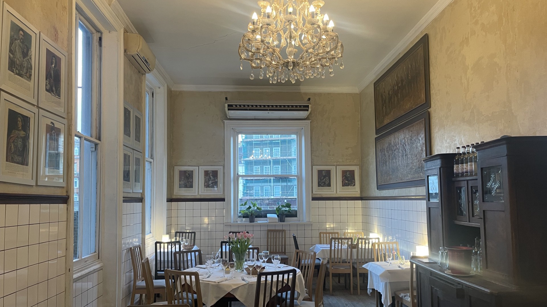 Enjoy Polish dishes in the elegant dining room at Daquise restaurant in South Kensington © Visit London/Jonny Payne. Tables with white tablecloths and traditional chairs in the dining room at Daquise, which also features white tiled walls and chandeliers.