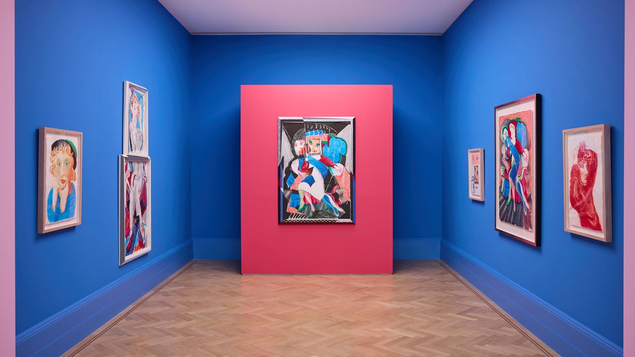 David Hockney: Living in Colour exhibition at Halcyon Gallery. Image courtesy of Halcyon Gallery. A gallery room with blue walls, parquet flooring and colourful David Hockney artworks, as part of the Living in Colour exhibition at Halcyon Gallery.