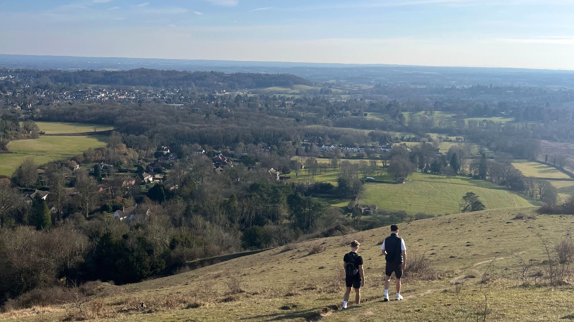 Sunny walks in the English countryside. Photo credit: Georgina Groom-Rietschy Two people walking along rolling hills in the english countryside.