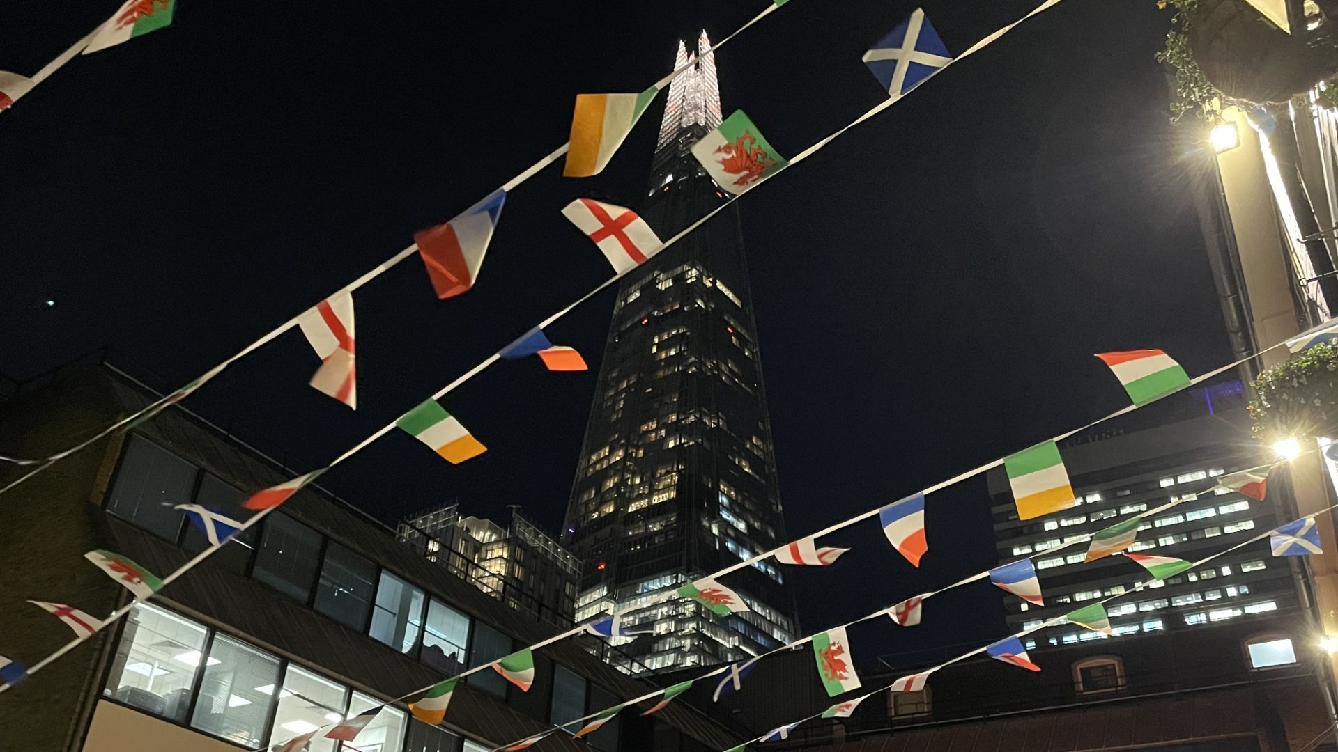 Enjoy a cool pint in a historic setting at The George Inn. Photo credit: Jonny Payne Flags of the world bunting against a night sky in London against the Shard.