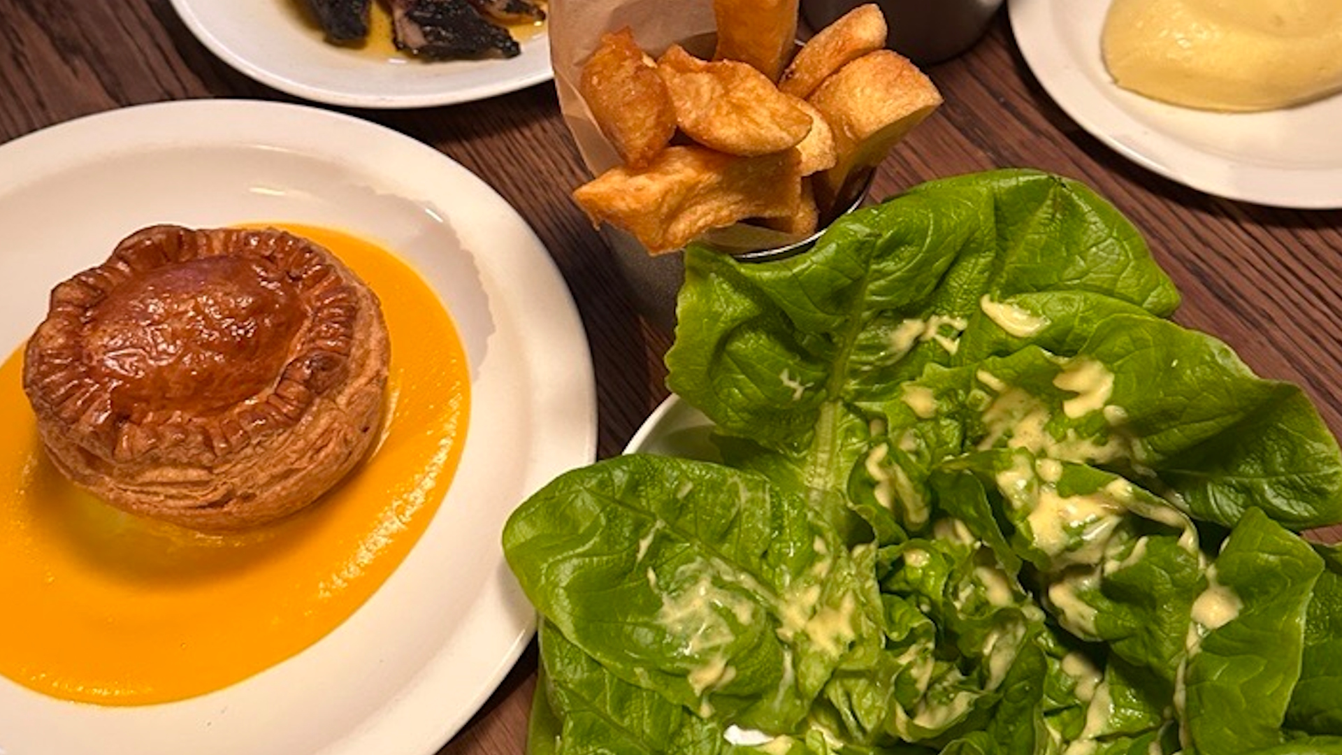 Tuck into pies and other gastropub fare at The Pelican © Visit London/Lucie Fryer. A pie with pumpkin puree on a white plate, a lettuce drizzled with dressing, and a bowl of chips at The Pelican.