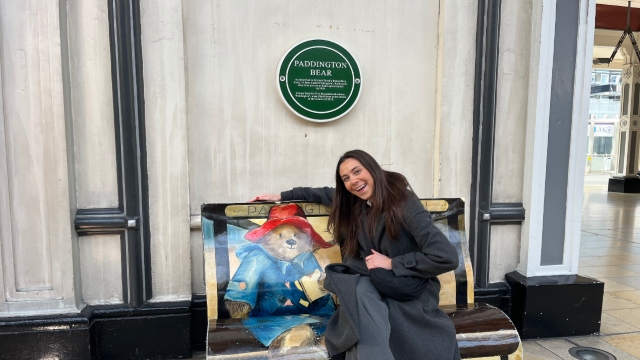A woman poses beneath the Paddington plaque in Paddington Station