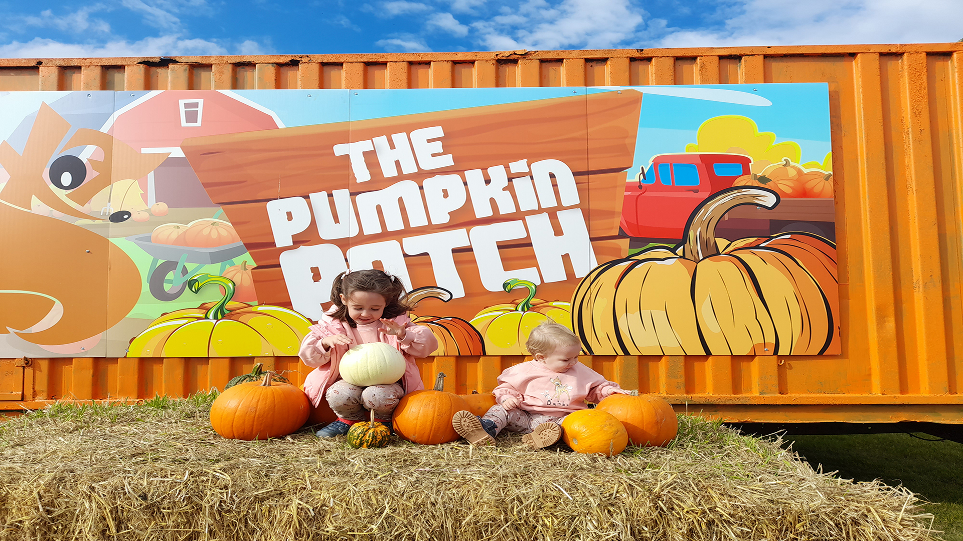 Take a trip with your loved ones to Foxes Farm. Image courtesy of Foxes Farm. A hay bale seating area with a toddler on it and some pumpkins and an orange shipping container behind it with the name of the farm on it.