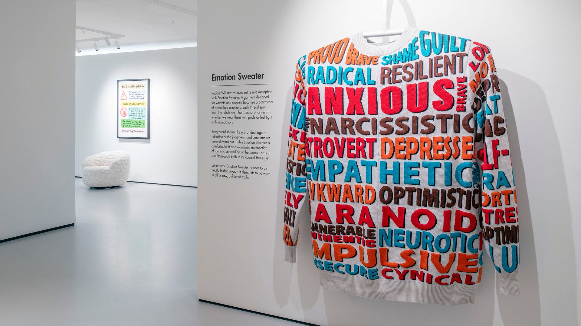 See Robbie Williams' personal experiences turned into striking art at Moco Museum. Image courtesy of Moco Museum. Large sweatshirt with bold taglines and armchair in background at Radical Honesty exhibition.