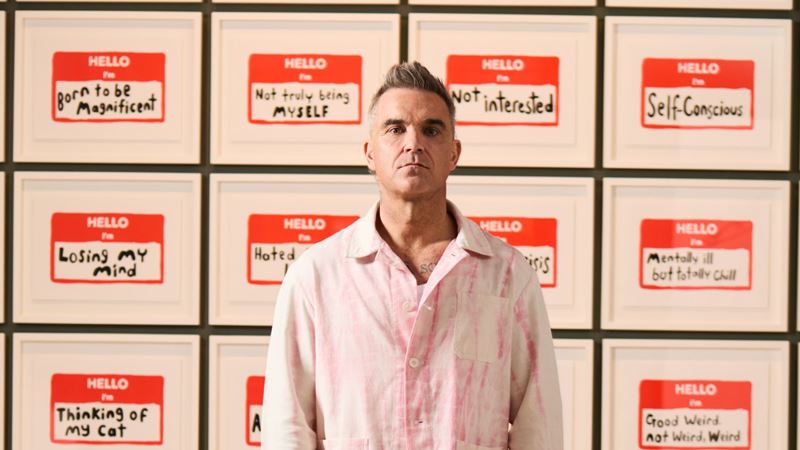 Robbie Williams standing in front of art exhibition wall at Moco Museum.