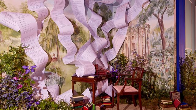 A wooden desk is set against a painted hall depicting the English countryside, with spirals of handwritten sheets emerging from the desk, as seen in the Sketch in Bloom exhibition.