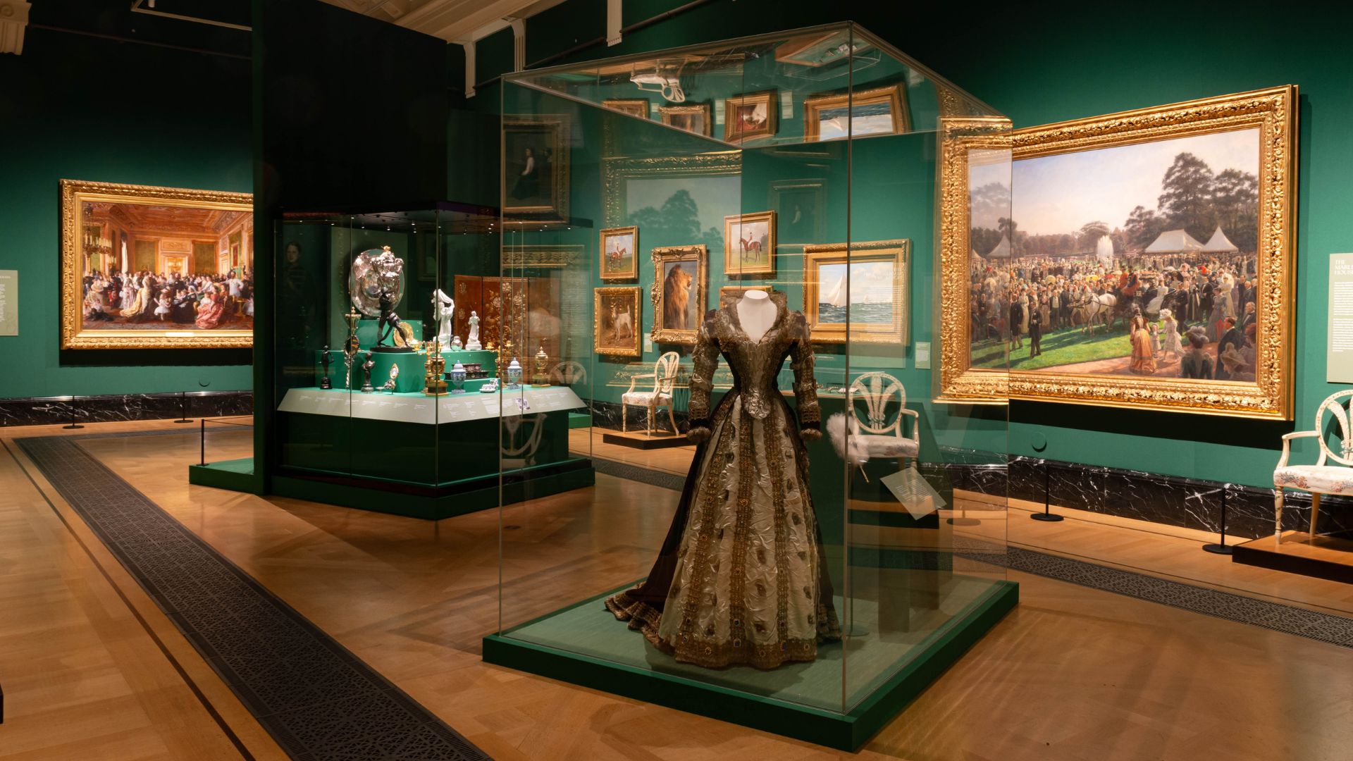 See more than 300 objects from the Royal Collection at The Edwardians: Age of Elegance. © Royal Collection Enterprises Limited 2025 | Royal Collection Trust. A dress and artwork reflecting the Edwardian royals in green gallery room.