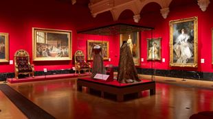 Coronation dresses in centre of red gallery room with several paintings surrounding.