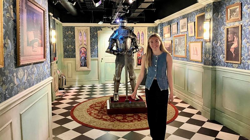 Person standing next to a steel knight in castle-inspired hallway at The Traitors: Live Experience.