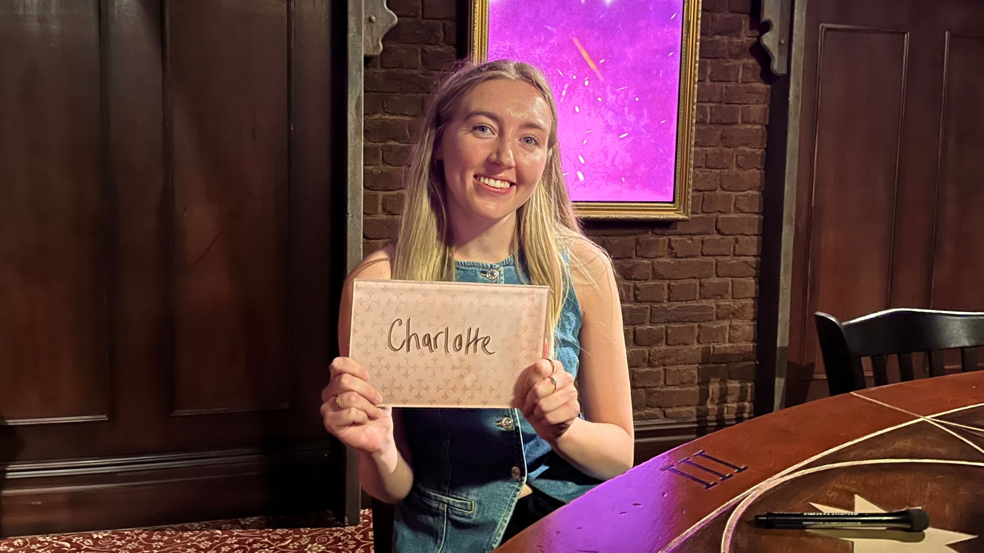 Proclaim your innocence as a Faithful at The Traitors: Live Experience. Image courtesy of Charlotte Pritchard. Person sitting a table holding up a name card with interactive screen in background.