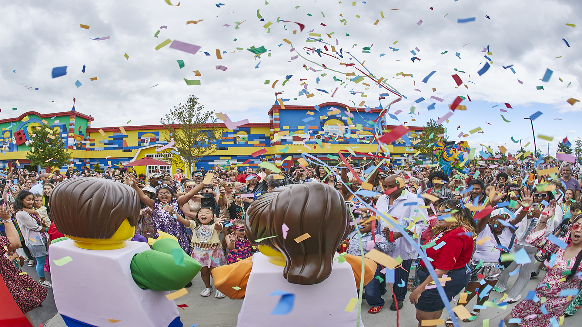 Celebrate LEGO Festival 2025. Image courtesy of Merlin Entertainment Two big Lego figures with a big Lego building in the background and a group of children in front facing the figures and confetti in the air.