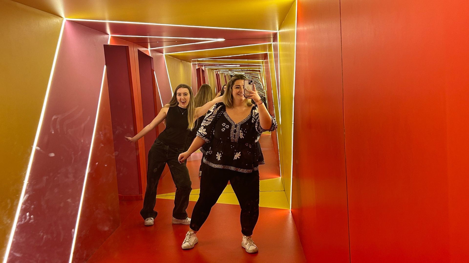 Explore the interactive exhibits at Twist Museum. © Visit London/Hannah Cornish two women smiling and posing for a photo in a mirror, in a slanted room giving the illusion of sliding movement