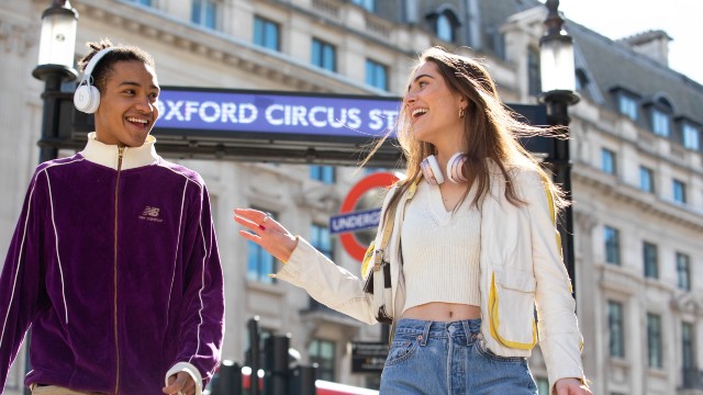 Two people smile at each other and laugh in front of a Tube station on Oxford Street in London.