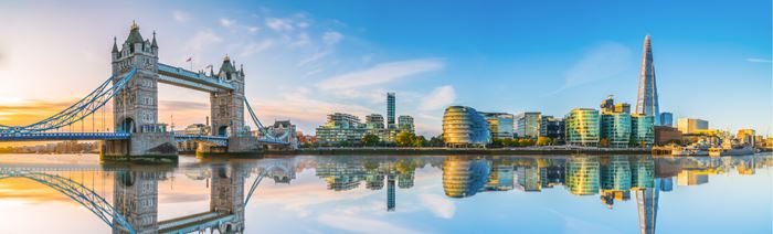 A photo of the London skyline during golden hour with Tower Bridge on the left and other famous buildings including The Shard with reflections on the river Thames in the foreground