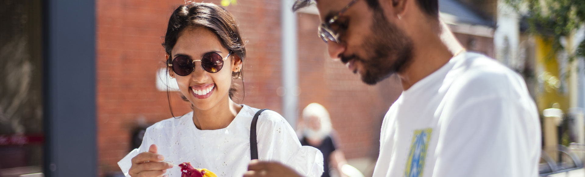 A photo of a man and woman smiling towards the camera with ice cream in their hands on a bright sunny day in London