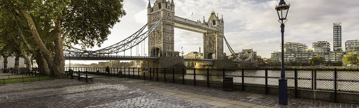 A cobbled riverside pathway in the foreground with Tower Bridge and the river Thames in the background.