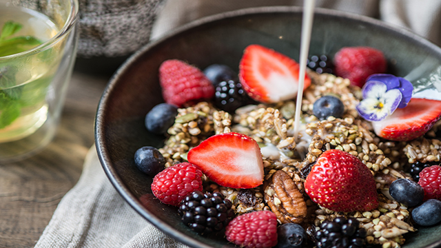 A bowl of mixed berries and granola with milk being poured in