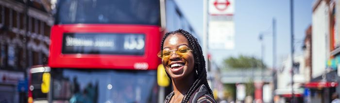 A woman stands in the streets of London while a red bus approaches.