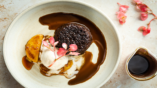 An aerial shot of sticky toffee pudding in a large bowl with a side of sauce