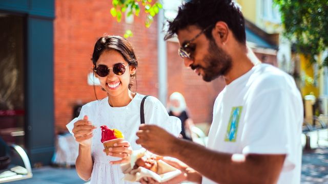 Two people in white tshirts and sunglasses eat ice creams on a sunny day in London.