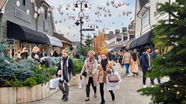 Three ladies walk through bicester village carrying shopping bags.