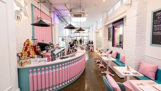 A bright pink and blue cafe with tables and chairs and a til covered in sweet treats at the Biscuiteers shop in london. 