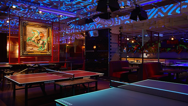 High-tech interactive ping pong at Bounce. Image courtesy of Bounce. A dark room with club-style lighting and ping pong tables laid out