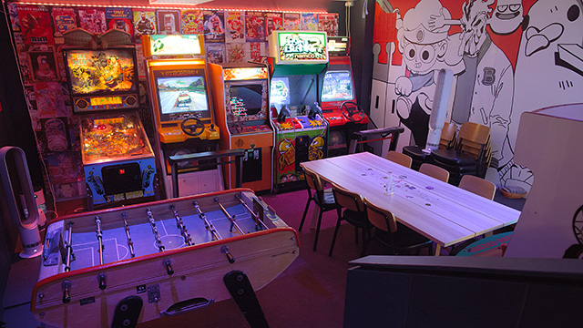 Loading Bar's dimly lit room filled with retro arcade games, a foosball table and table with chairs to enjoy drinks from the bar.
