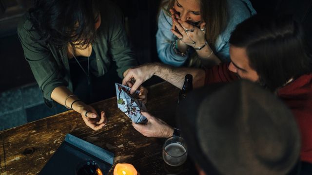 Moriarty's Game. Image courtesy of Hidden City. A group of people sit at a brown table holding clues to an escape room.