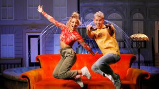 two people jumping up in the air in front of a red sofa