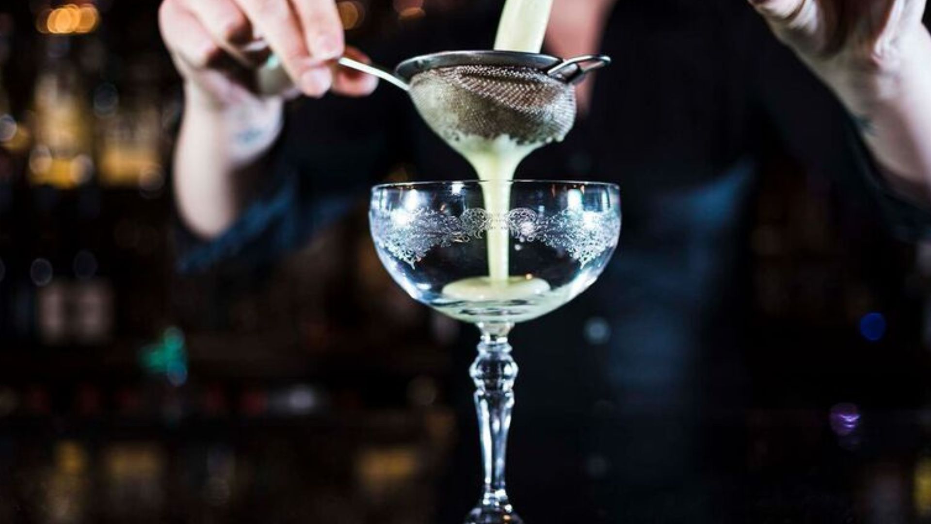 Cocktail masterclass in London. Image courtesy of Red Letter Days. a person pouring a cocktail through a strainer into a glass