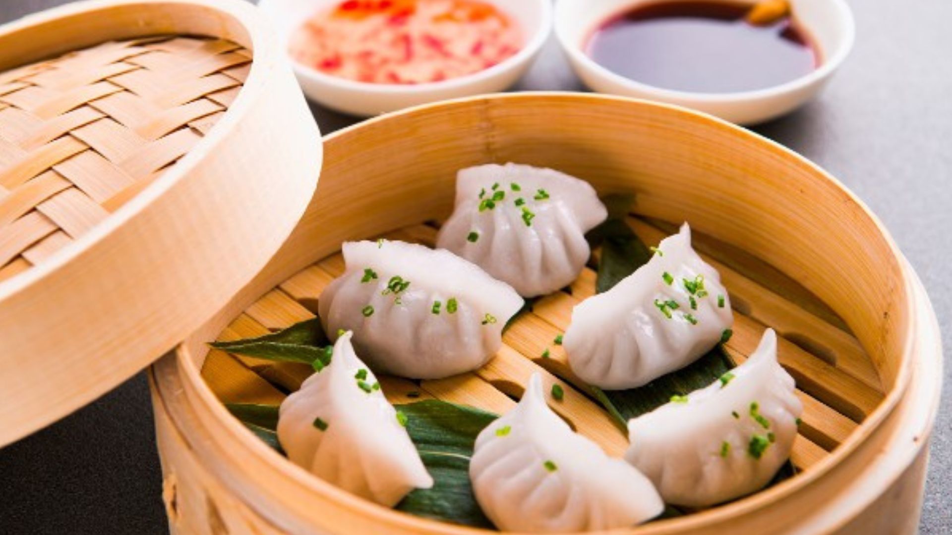 Dim sum cooking class in London. Image courtesy of Red Letter Days. Prawn dumplings in a wooden basket with dipping sauces in the background.