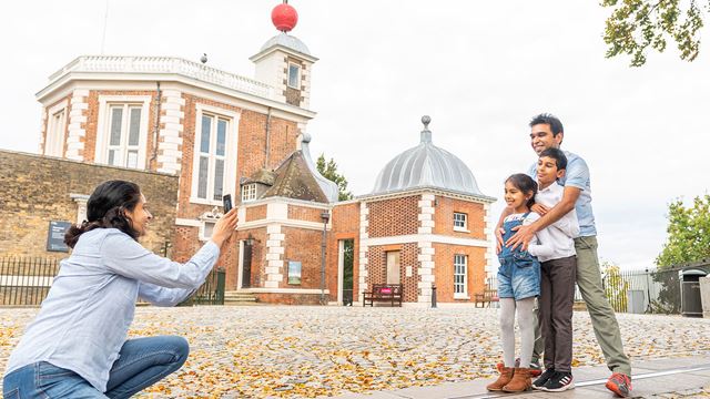 A mum kneeling to take a photo of her kids and partner in front of the Royal Observatory, Greenwich.