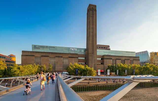 A family and others walk across the bridge opposite the London Gallery Tate Modern.