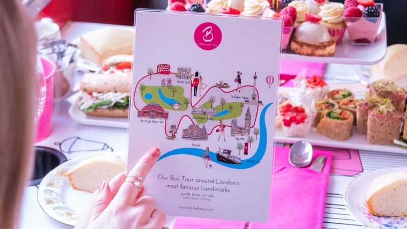 A person pointing at a route map for an afternoon tea bus tour, with plates of sweet and savoury treats in the background