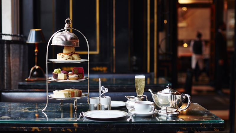 Savour champagne and scrumptious food, from breakfast to dinner and afternoon tea, at The Wolseley. Credit: The Wolseley. Image courtesy of The Wolseley. Three-tiered afternoon tea stand with cakes, scones and sandwiches, alongside pot of tea and glass of champagne on green marble table at The Wolseley.