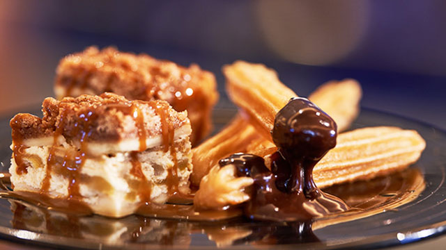 Close-up of churros covered in dark chocolate and mini pies covered in caramel.