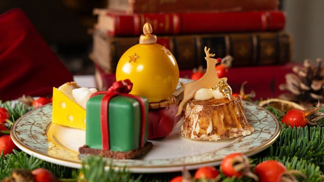 festive afternoon tea sweet treats presented on a small white plate, including cake shaped like a gold bauble and a green christmas present with a red bow