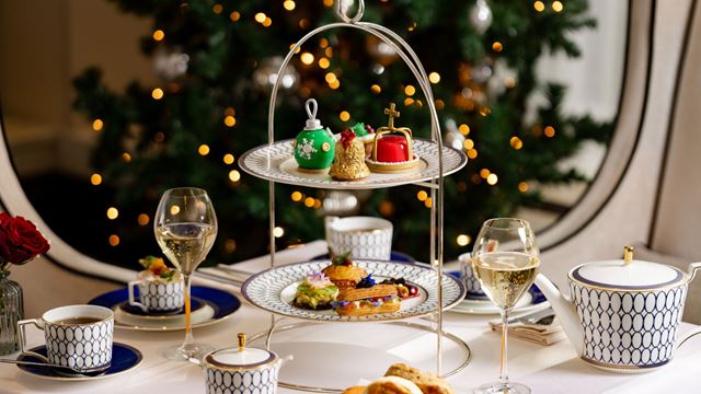 festive afternoon tea presented on a white cloth table with fine china tea cups and a lit Christmas tree in the background