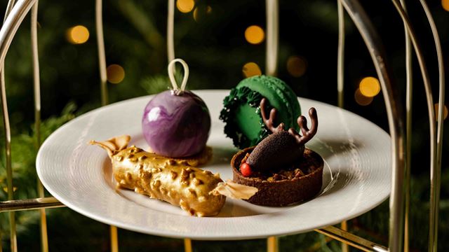 a small round plate with christmas themed afternoon tea patisserie treats, with fairy lights in the background