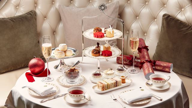 white table cloth small table with a festive afternoon tea stand, small plates of finger sandwiches and tea cups, christmas crackers decorating the table